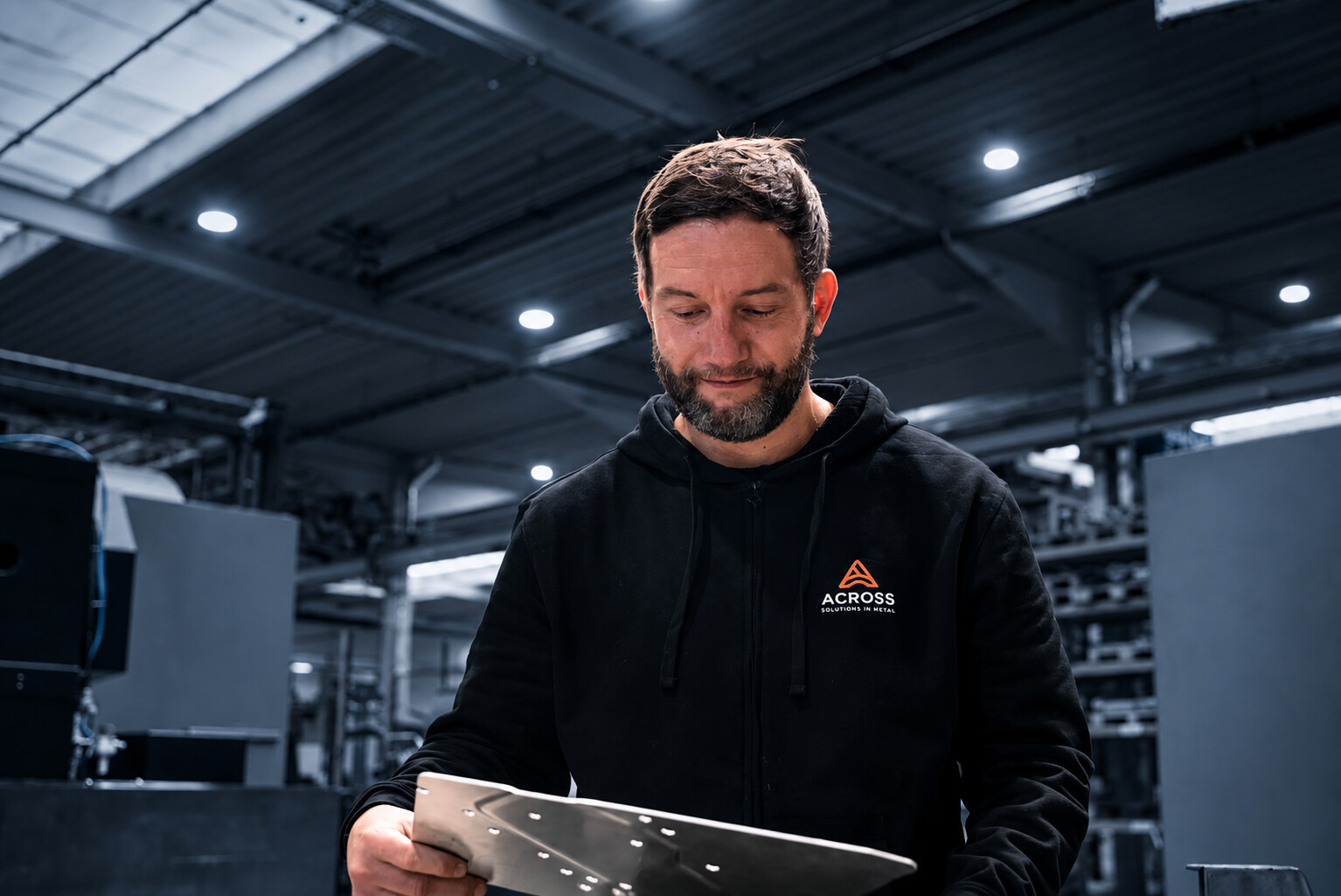 Mitarbeiter prüft ein Metallbauteil bei ACROSS Solutions in Metal.