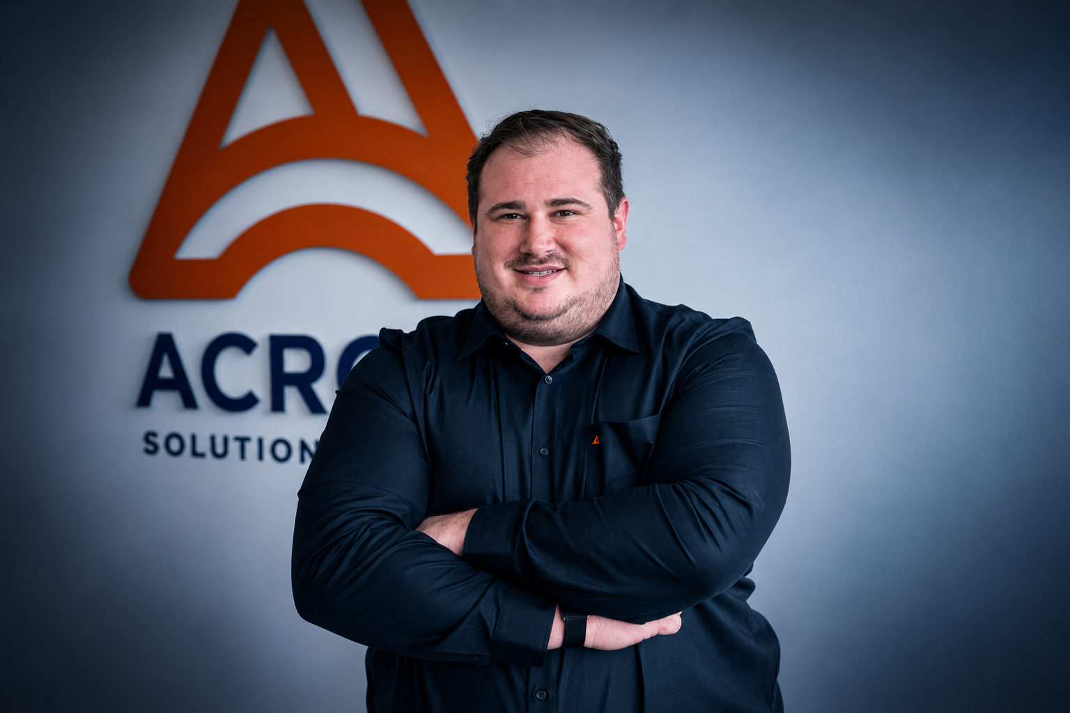Kevin Eberhardt, Geschäftsführer von ACROSS Solutions in Metal, mit verschränkten Armen vor dem Firmenlogo.