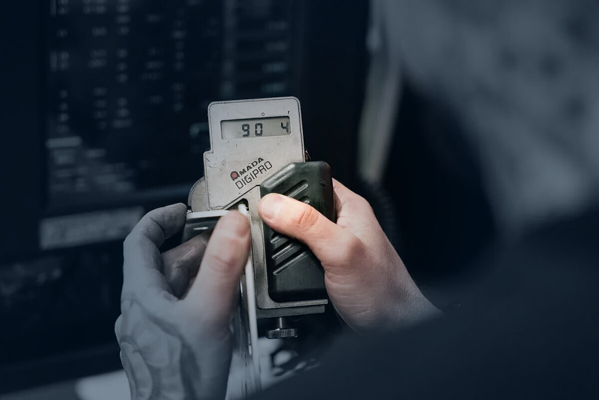 Mitarbeiter prüft ein Metallbauteil mit einem AMADA DIGIPRO Messgerät.